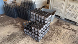 Stacks of black plastic trays with cylindrical objects on a concrete floor.